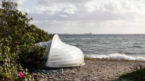 En vit båt vid en stenig strand med hav och molnig himmel i bakgrunden
