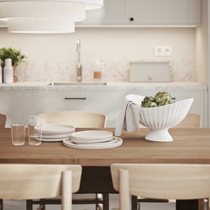 Modern köksinteriör med ett träbord, tallrikar, glas och en vit dekorativ skål med grönsaker. Ljus inredning med marmordetaljer och neutrala färger