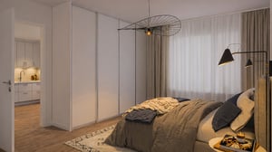Sovrum med en dubbelsäng, beige gardiner, taklampa och golvlampa. En dörr leder till ett kök med ljusa skåp och träfärgat golv