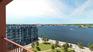 Utsikt över sjö, bostadshus och innergård med gräsmatta och träd