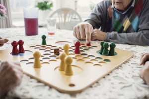Äldre person spelar sällskapsspel vid ett bord i ett ljust rum