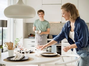 Två personer dukar fram i ett modernt kök med vit inredning