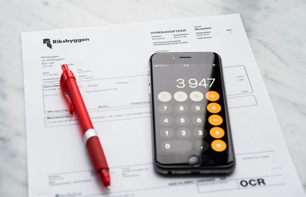 Räkning från Riksbyggen på ett bord med en röd penna och en smartphone som visar en kalkylator med siffran 3947
