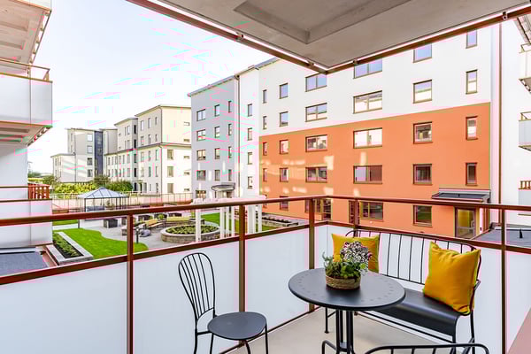 Balkong med utemöbler och utsikt över en innergård med grönområden och moderna flerfamiljshus i bakgrunden