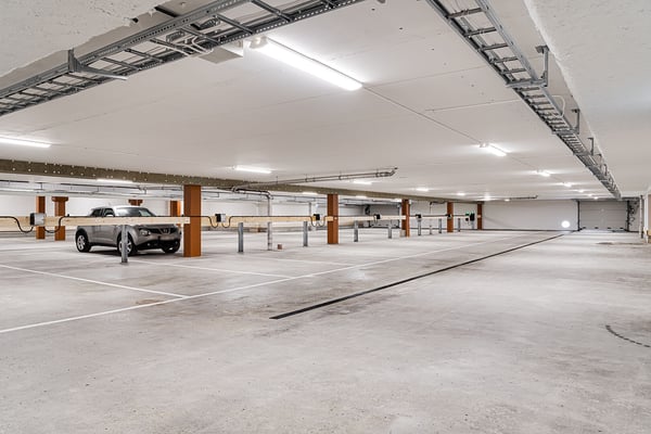 Modern parkeringsgarage med bilar parkerade vid laddstationer och ljus från taklampor