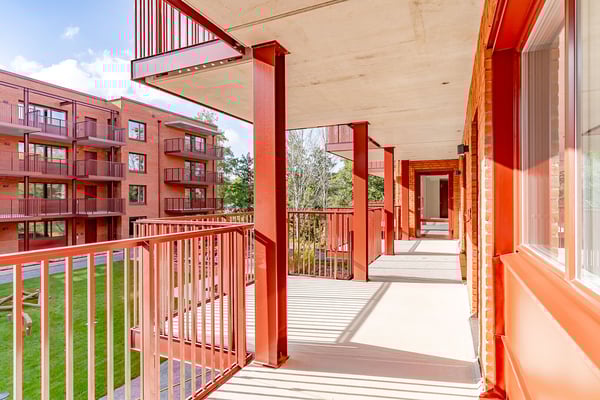 Balkong med röda räcken och utsikt över grönområde samt moderna byggnader i tegel
