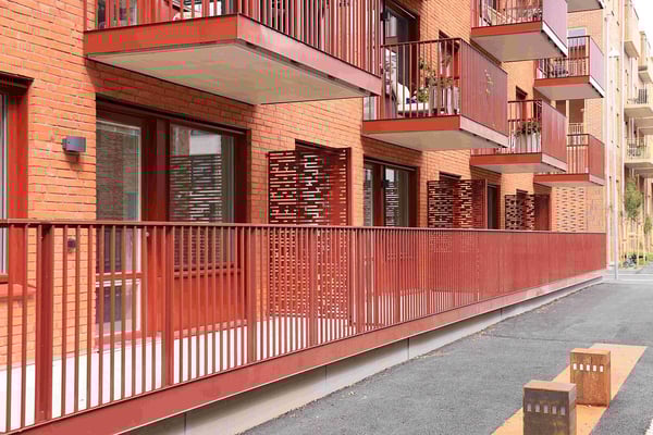 Flera lägenhetsbalkonger med röda räcken och tegelväggar på ett bostadshus
