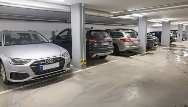Bilar parkerade i en underjordisk parkeringsgarage med gråa betongväggar och vått golv