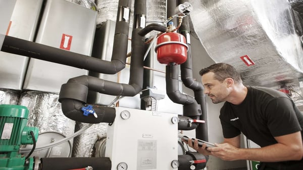 En tekniker arbetar med rör och ventilationssystem i ett industriellt maskinrum