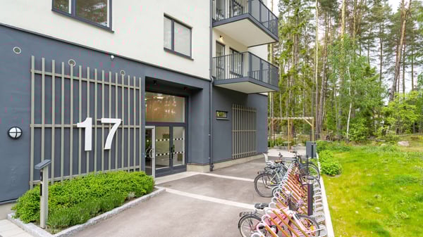 Flerbostadshus med nummer 17, entré och cykelparkering vid grönskande skogsmiljö