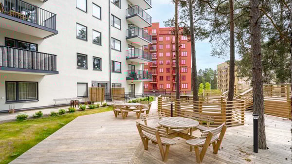 Innergård med träaltan, sittgrupper och flerfamiljshus i vitt och rött