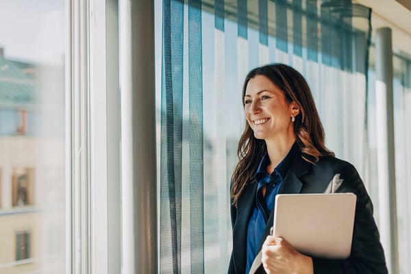 Porträtt av en kvinna i blazer som håller en surfplatta vid ett fönster