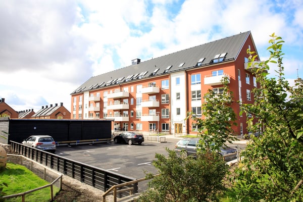 Rött flerfamiljshus med balkonger och parkeringsplats utanför