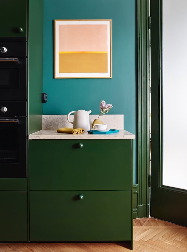Kök med gröna skåp, ljus bänkskiva och detaljinredning