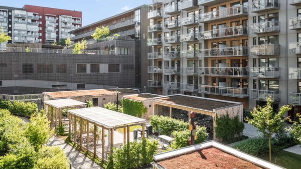 Bostadsgård med moderna flerbostadshus, balkonger och gröna pergolor i soligt väder