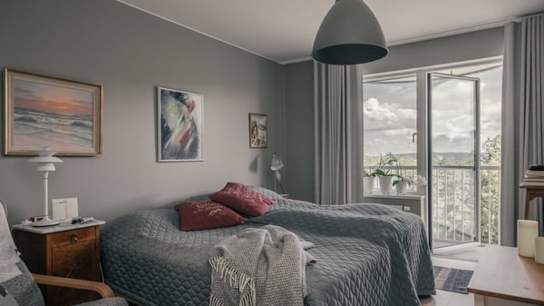 Sovrum med bäddad dubbelsäng, grå väggar och öppen balkongdörr mot utsikten