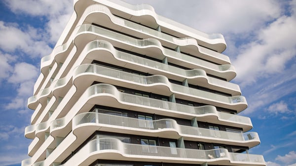 Modernt bostadshus med vita, vågformade balkonger mot blå himmel