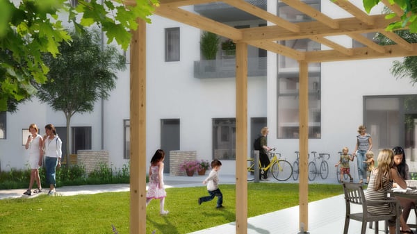 Personer går och umgås i en grön innergård mellan vita bostadshus