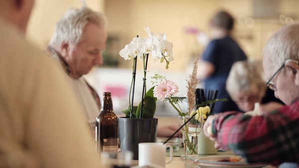 Personer sitter vid ett bord med blommor och dryck på en inomhusplats