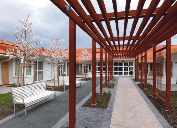 Gårdsmiljö med pergola, bänkar och blommande träd framför bostadshus