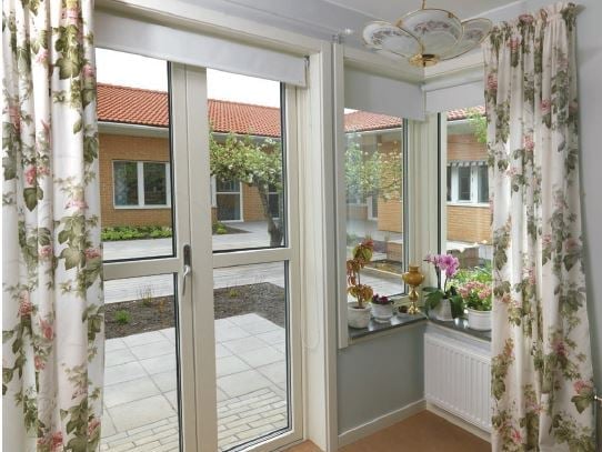 Inglasad uteplats med dörr, stora fönster och blomsterprydda gardiner