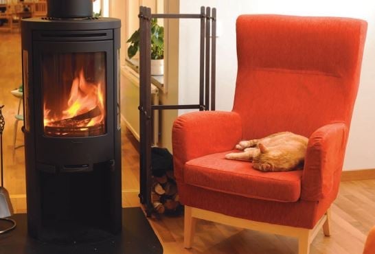 Röd fåtölj bredvid en tänd braskamin i ett vardagsrum