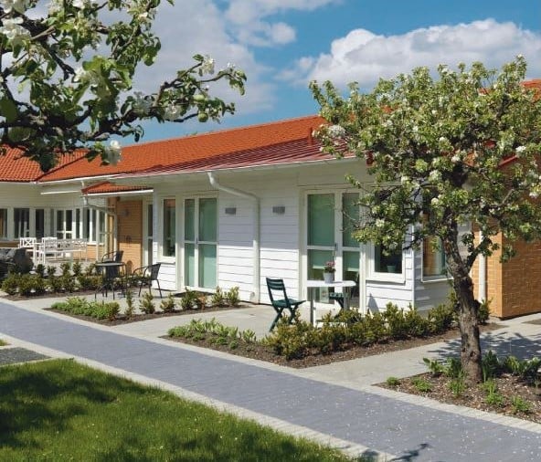 Lägenhet med uteplats och trädgård framför ett vitt hus med rött tak