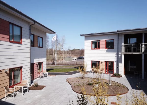 Tomt gårdsmiljö mellan två flerbostadshus med uteplatser och röda fönsterkarmar