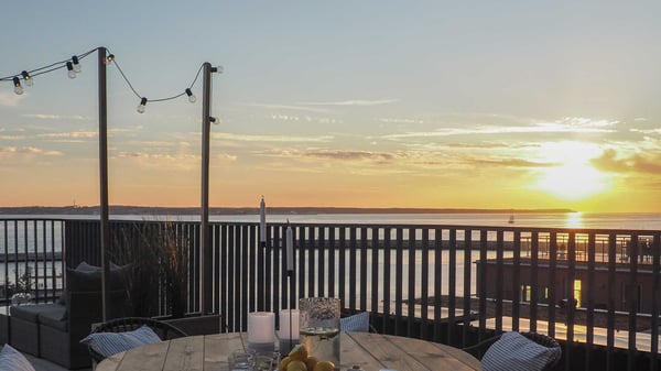 Uteplats med sittgrupp, runda bord och utsikt över vatten i solnedgång