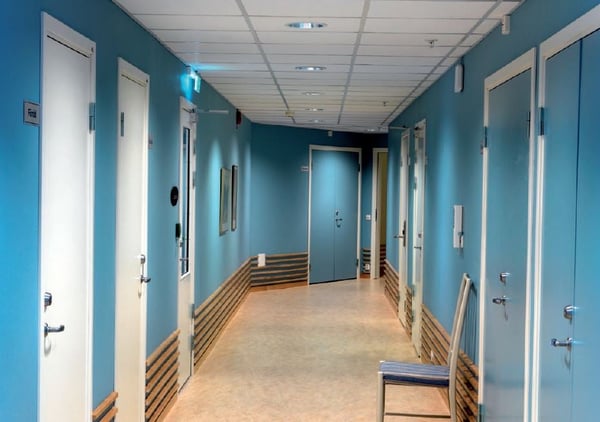 Korridor med blå väggar, vita dörrar och en stol i korridoren