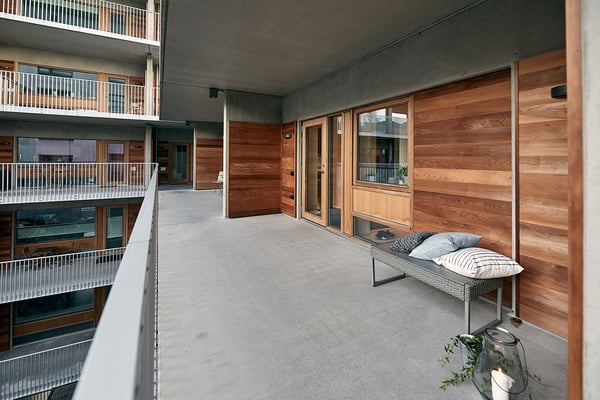 Balkong med träpanel, glasdörrar och sittbänk med kuddar