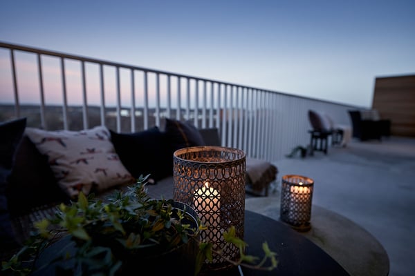 Uteplats med tända ljuslyktor, kuddar och växter i kvällsljus