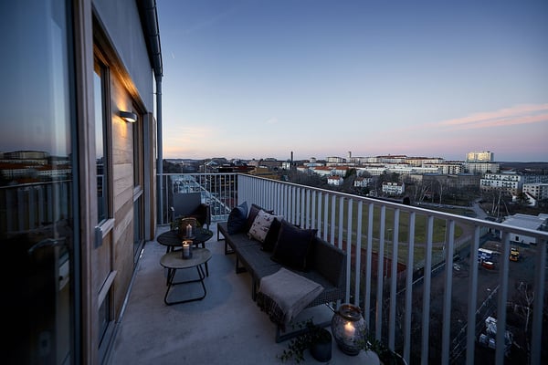 Balkong med utsikt över stad vid skymning, möblerad med soffa, bord och lyktor
