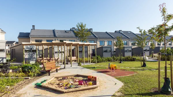 Innegård vid bostadsområde med lekplats, sandlåda, pergola, bänkar och radhus i bakgrunden