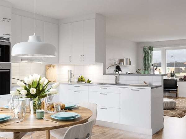 Modernt vitt kök med matplats, runda matbordet dukat för flera personer och stora fönster mot vardagsrum