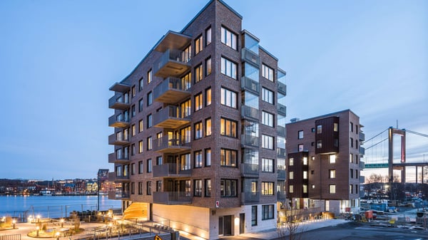 Flerbostadshus vid vattnet i skymning, med upplysta fönster och balkonger