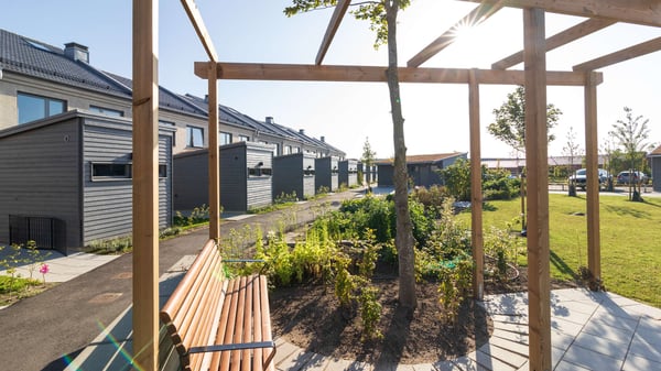 Uteplats med träpergola, bänk och grönytor vid moderna radhus
