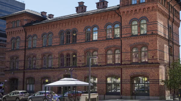 Fasad av en röd tegelbyggnad med många välvda fönster och parkerade bilar framför