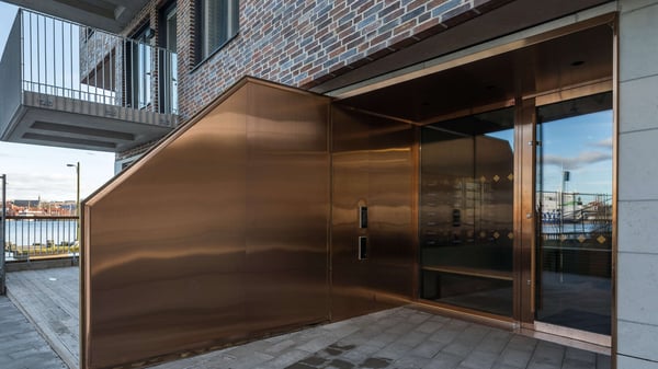 Entré till flerbostadshus med kopparfärgad fasad och glasdörrar
