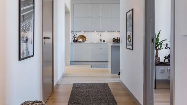Köksinteriör i en modern lägenhet med ljusa skåp, trägolv och en lång hall