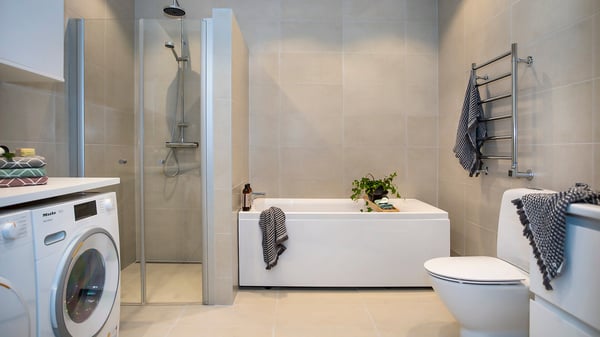 Modernt badrum med dusch, badkar, tvättmaskin och toalett i ljusa neutrala toner