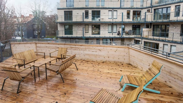 Lägenhet med trädäckad uteplats och sittgrupp i trä, omgiven av flerbostadshus