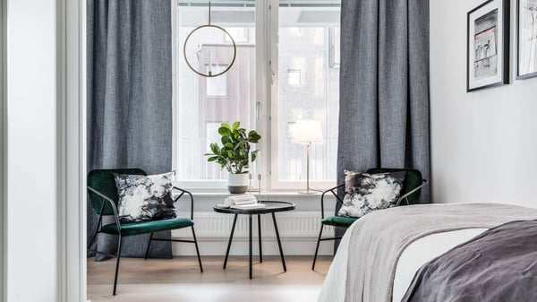 Inflyttningsklar lägenhet med stilren inredning, två gröna fåtöljer och fönster med mörka gardiner
