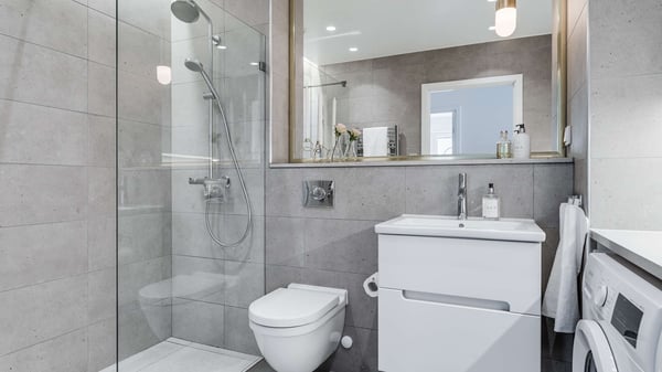 Modernt badrum med duschhörna i glas, vägghängd toalett och handfat med spegel