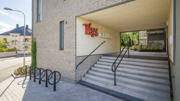 Entré med trappa under ett bostadshus med tegel фасad, cykelställ och skylt i rött och vitt