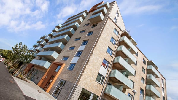 Flerfamiljshus med balkonger i ljus tegel, fotograferat nerifrån mot blå himmel