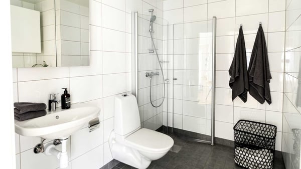 Modernt badrum med vit kakelvägg, dusch, toalett och handfat