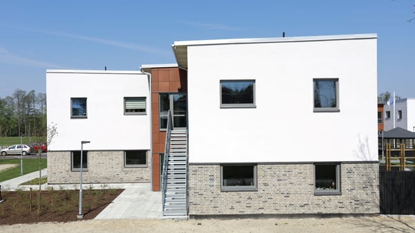 Flerbostadshus med vit fasad och gråtegel, sett utifrån