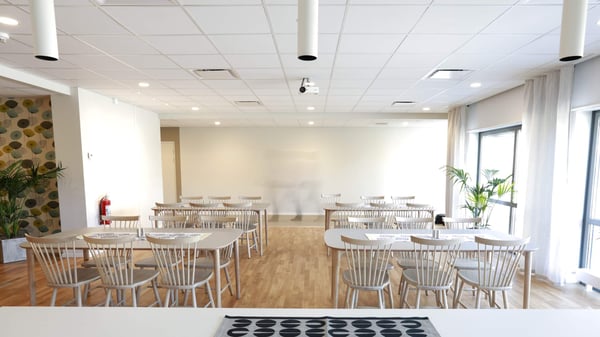 Matsal med ljusa ytor, trägolv och bord med stolar