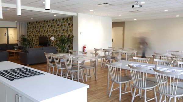 Tomt rum med matbord och stolar i en ljus gemensamhetslokal